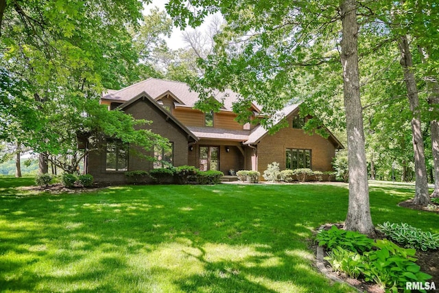 view of front of property featuring a front yard, brick siding, and roof with shingles
