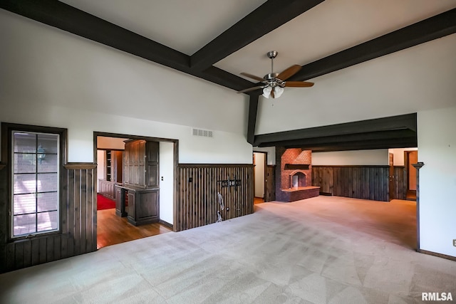unfurnished bedroom with a brick fireplace, carpet floors, beam ceiling, a wainscoted wall, and a high ceiling