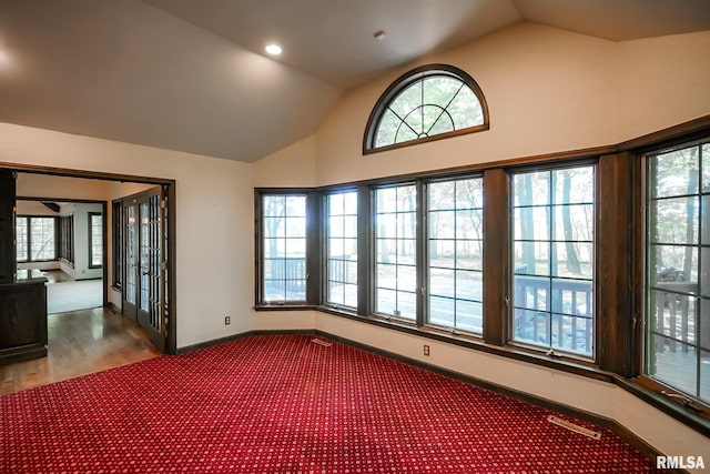 unfurnished room with lofted ceiling, carpet flooring, baseboards, and plenty of natural light