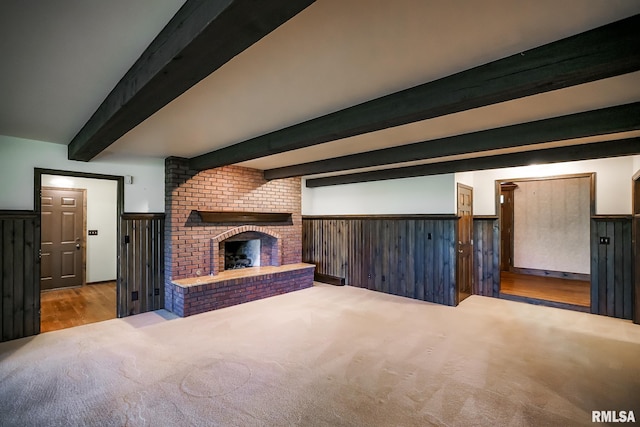 unfurnished living room featuring a wainscoted wall, beamed ceiling, carpet, and a fireplace
