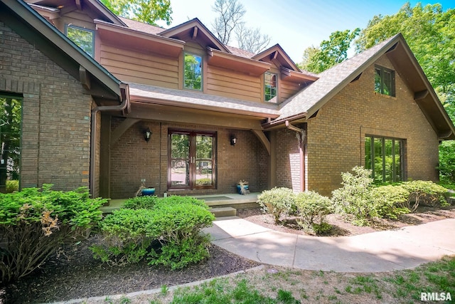 doorway to property with brick siding, a porch, and a shingled roof