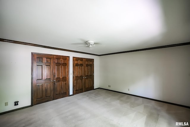 unfurnished bedroom featuring multiple closets, baseboards, ornamental molding, light colored carpet, and a ceiling fan