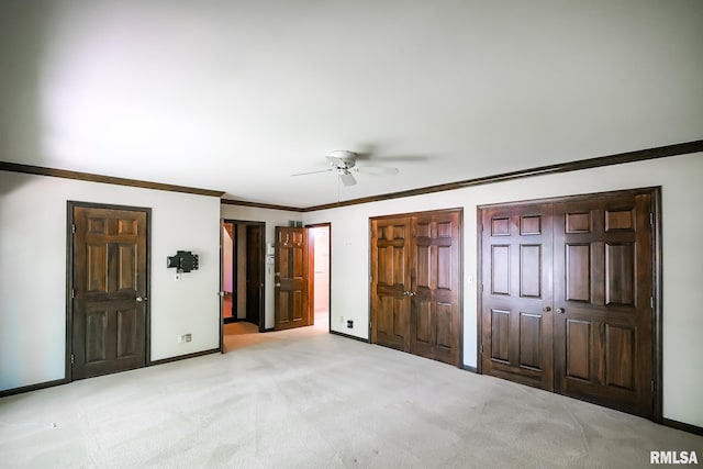 unfurnished bedroom with carpet flooring, baseboards, two closets, crown molding, and a ceiling fan