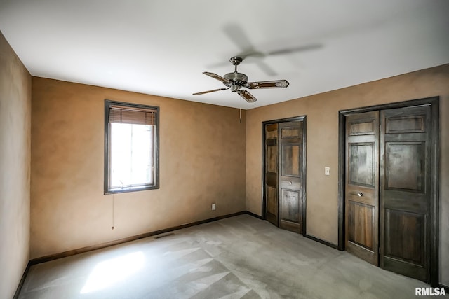 unfurnished bedroom featuring baseboards, light carpet, two closets, and a ceiling fan