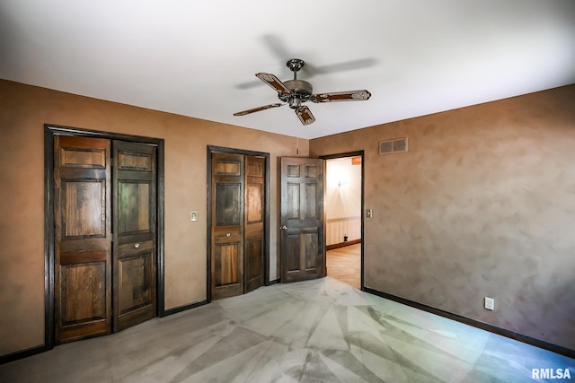 unfurnished bedroom featuring multiple closets, light colored carpet, baseboards, and a ceiling fan