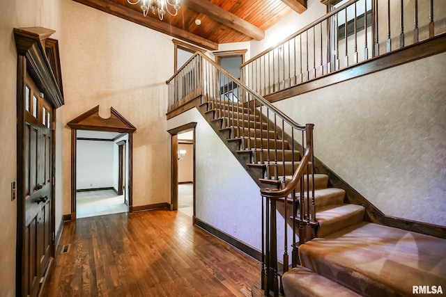 stairway with a chandelier, beamed ceiling, wooden ceiling, hardwood / wood-style flooring, and baseboards