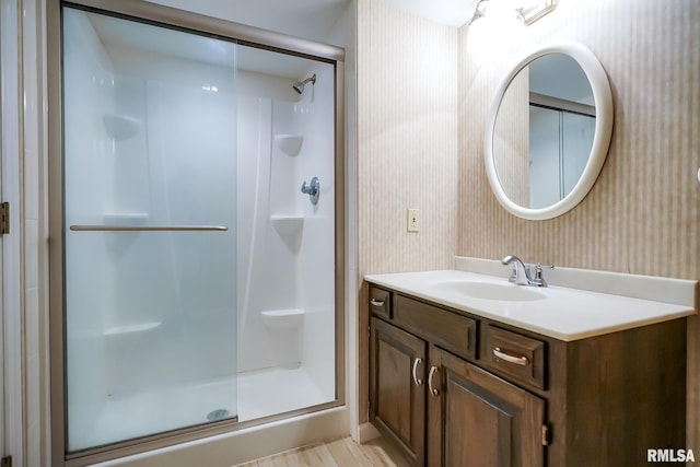full bathroom featuring wallpapered walls, a shower stall, and vanity