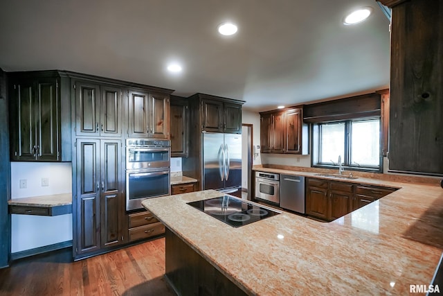 kitchen featuring appliances with stainless steel finishes, a sink, light wood finished floors, light stone counters, and recessed lighting