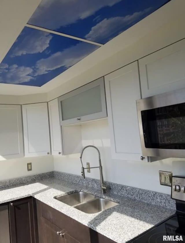 125 SW Jefferson Ave Unit W4S, Peoria, IL 61602 - kitchen with stainless steel appliances, a sink, dark brown cabinetry, white cabinetry, and light stone countertops