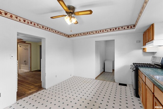 507 E Main St, Bryant, IL 61519 - kitchen featuring stainless steel range with gas stovetop, ceiling fan, light flooring, dark countertops, and brown cabinets