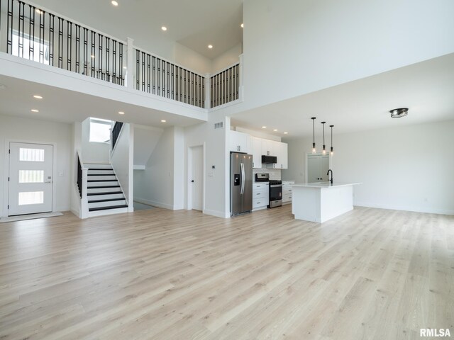112 Shannon Hills Dr, Washington, IL 61571 - unfurnished living room with stairs, a towering ceiling, light wood finished floors, a sink, and baseboards