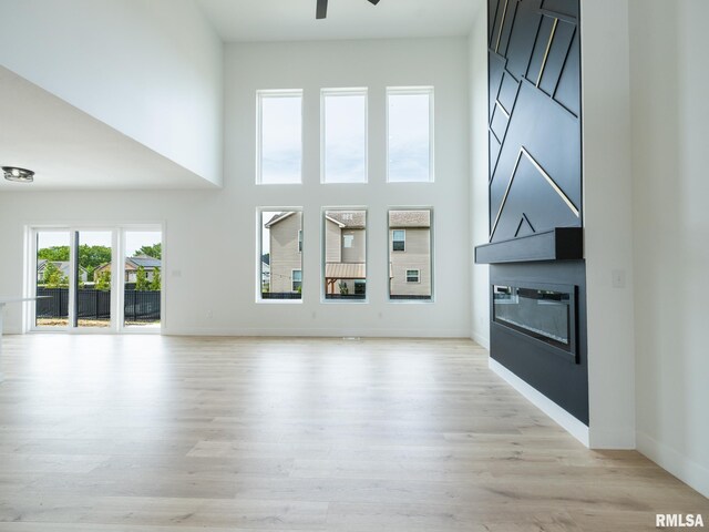 112 Shannon Hills Dr, Washington, IL 61571 - unfurnished living room featuring a large fireplace, a ceiling fan, light wood finished floors, baseboards, and a towering ceiling