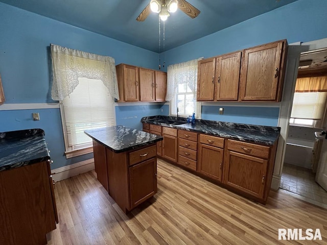 102 W 1st St, Table Grove, IL 61482 - kitchen featuring a ceiling fan, light wood-type flooring, brown cabinetry, a center island, and dark stone countertops