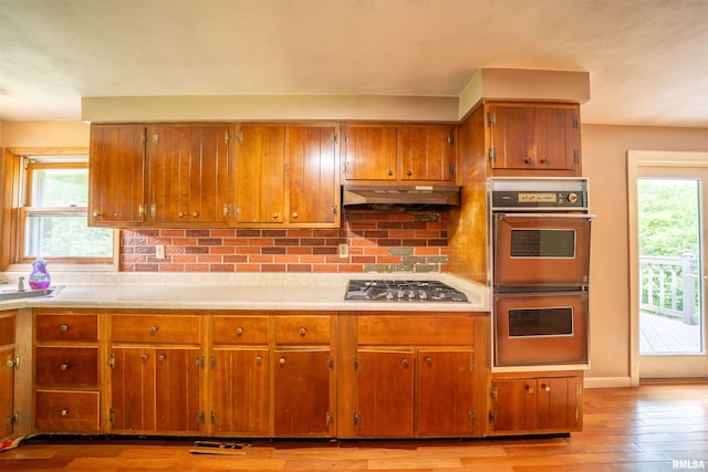 23907 Veterans Rd, Morton, IL 61550 - kitchen featuring stainless steel gas cooktop, double wall oven, brown cabinetry, under cabinet range hood, and light countertops