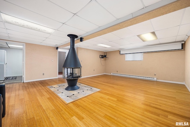 4517 W Hetherwood Dr, Peoria, IL 61615 - basement featuring a baseboard heating unit, a wood stove, wood finished floors, baseboards, and a paneled ceiling