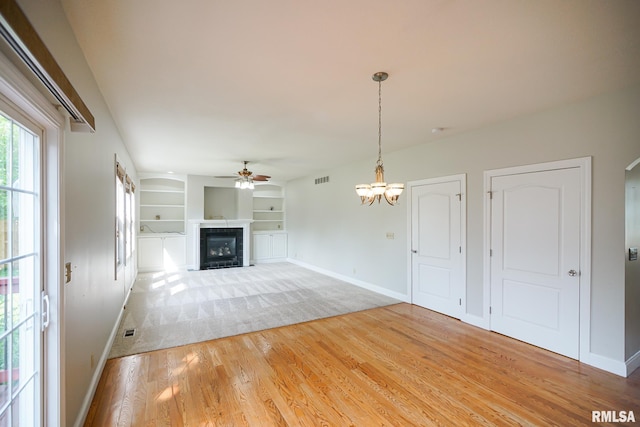 521 S French Dr, Dunlap, IL 61525 - unfurnished living room featuring a ceiling fan, a fireplace, light wood-style floors, built in features, and a chandelier