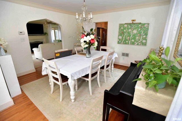 3307 N Biltmore Ave, Peoria, IL 61604 - dining room with light wood-style flooring, arched walkways, ornamental molding, a chandelier, and a fireplace