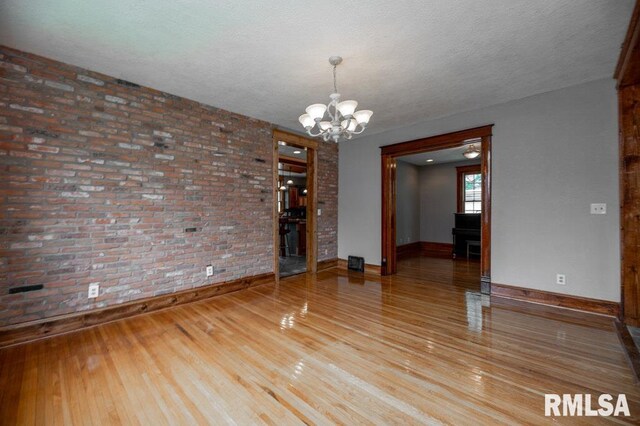 307 N Logan St, Deer Creek, IL 61733 - unfurnished room with brick wall, a chandelier, wood finished floors, baseboards, and a textured ceiling