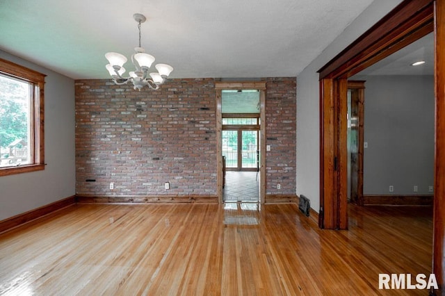 307 N Logan St, Deer Creek, IL 61733 - unfurnished room with a chandelier, plenty of natural light, brick wall, baseboards, and light wood-style flooring