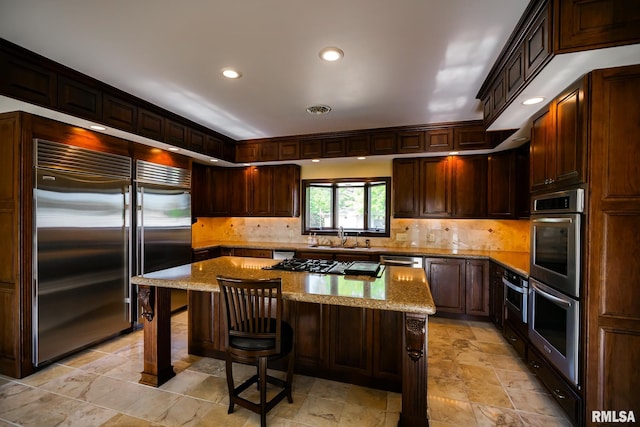 241 Birch Pl, Kewanee, IL 61443 - kitchen with appliances with stainless steel finishes, a kitchen bar, tasteful backsplash, a kitchen island, and light stone finish flooring