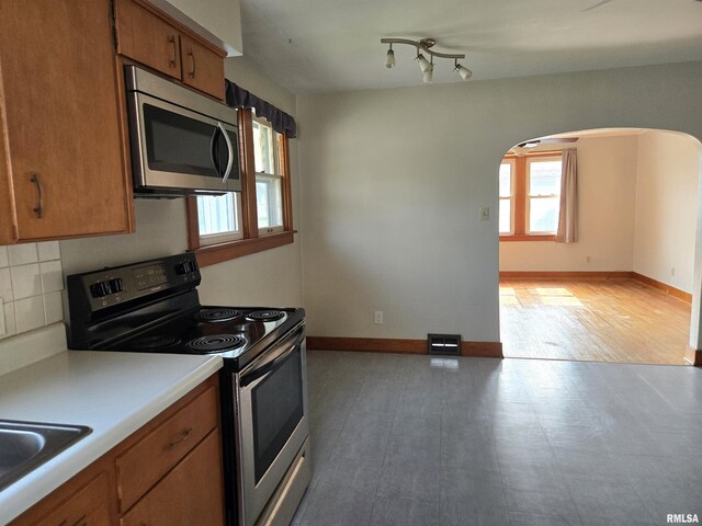 904 E Elm St, Canton, IL 61520 - kitchen featuring electric range oven, stainless steel microwave, brown cabinetry, arched walkways, and backsplash