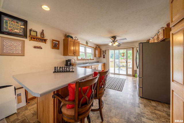21501 N Berchtold Rd, Chillicothe, IL 61523 - kitchen featuring freestanding refrigerator, stone tile flooring, a peninsula, a ceiling fan, and light countertops