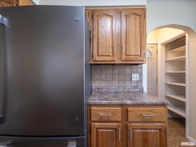 621 E Sciota Ave, Peoria Heights, IL 61616 - kitchen featuring freestanding refrigerator, tasteful backsplash, brown cabinetry, and arched walkways