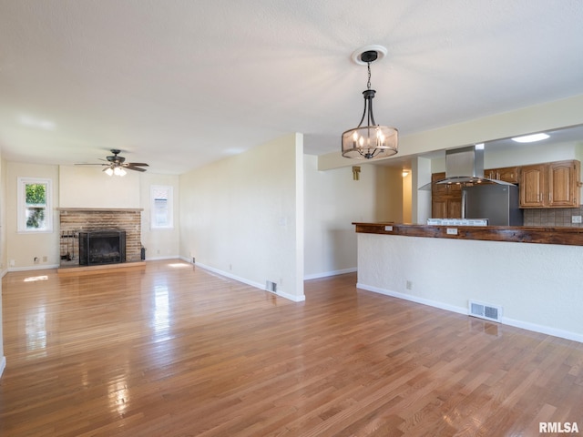 621 E Sciota Ave, Peoria Heights, IL 61616 - unfurnished living room with a fireplace with raised hearth, light wood-type flooring, a ceiling fan, and a chandelier