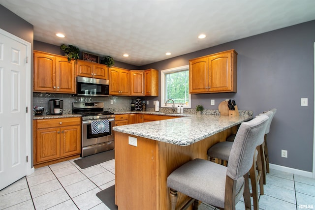 116 Field Ct, East Peoria, IL 61611 - kitchen featuring stainless steel appliances, a peninsula, a kitchen breakfast bar, light stone countertops, and brown cabinetry