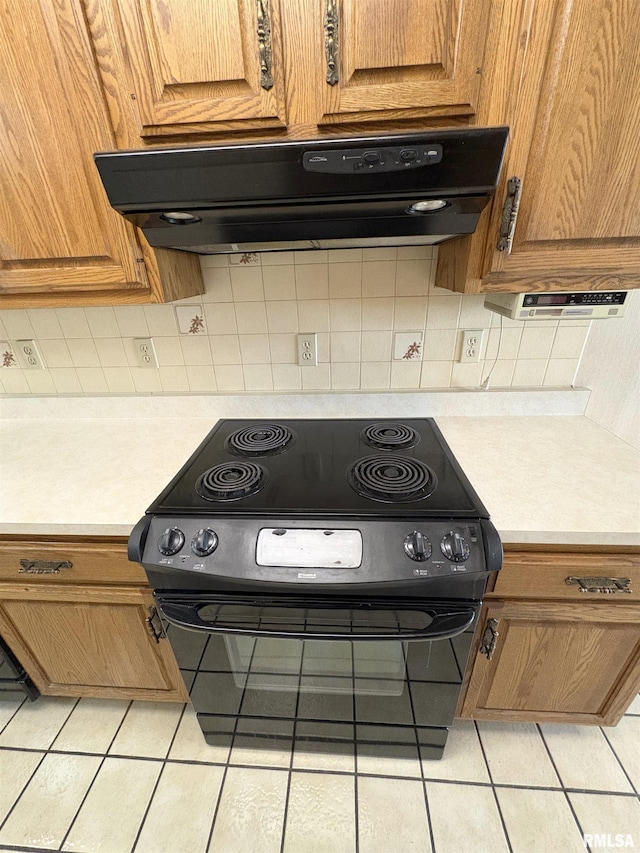 502 W Crestwood Dr, Peoria, IL 61614 - kitchen with black range with electric stovetop, light tile patterned floors, range hood, light countertops, and brown cabinetry