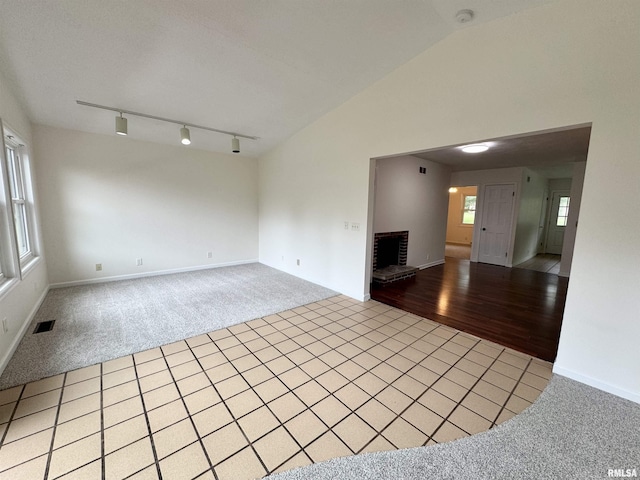 133 Holden Dr, Macomb, IL 61455 - unfurnished living room featuring light carpet, light tile patterned floors, track lighting, vaulted ceiling, and a fireplace
