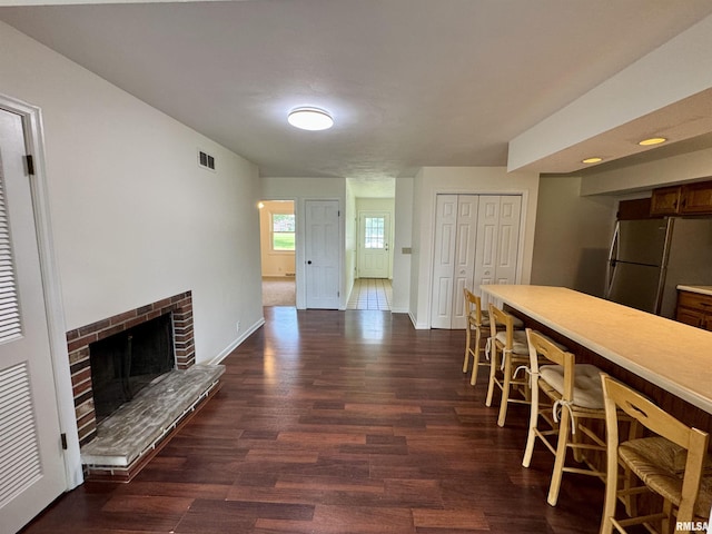 133 Holden Dr, Macomb, IL 61455 - kitchen featuring freestanding refrigerator, a breakfast bar, dark wood-style floors, a brick fireplace, and light countertops