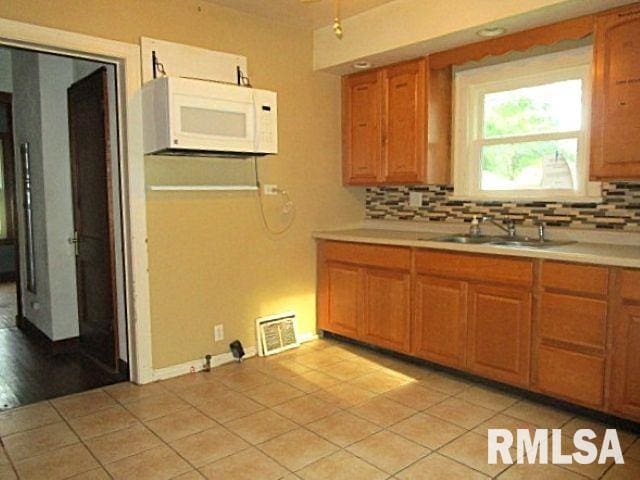 320 E Meadow Lawn St, Manito, IL 61546 - kitchen with white microwave, light countertops, decorative backsplash, brown cabinets, and light tile patterned floors