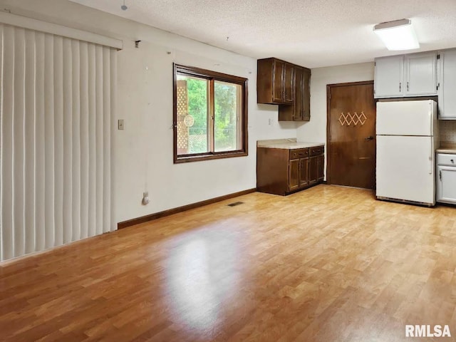 1003 Tonti Rd, Toulon, IL 61483 - kitchen with freestanding refrigerator, light wood-style flooring, a textured ceiling, light countertops, and dark brown cabinets