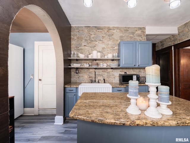 405 Washington St, Pekin, IL 61554 - kitchen featuring blue cabinetry, arched walkways, dark wood-style flooring, open shelves, and light stone counters