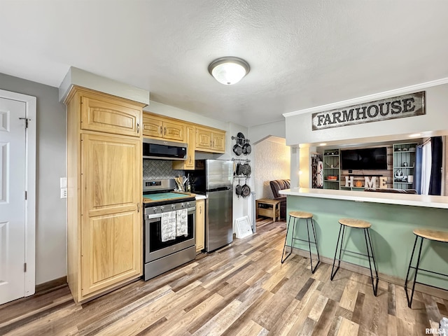 1506 S Capitol St, Pekin, IL 61554 - kitchen featuring stainless steel appliances, a breakfast bar area, light brown cabinets, light wood-style flooring, and backsplash