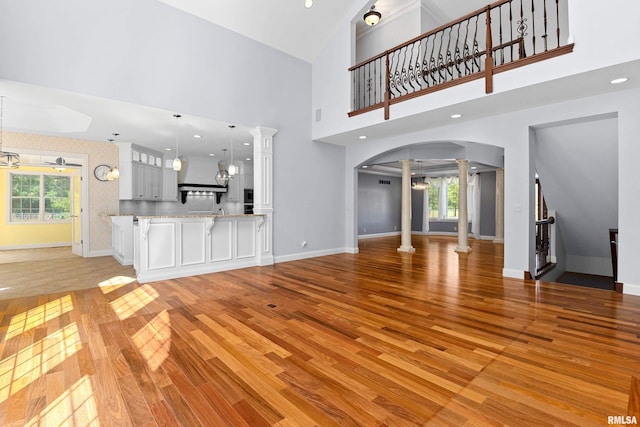 4851 Sheridan Rd, Groveland, IL 61535 - unfurnished living room featuring decorative columns, light wood finished floors, plenty of natural light, arched walkways, and a high ceiling