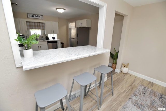 4527 N Nelson Dr, Peoria, IL 61614 - kitchen with appliances with stainless steel finishes, a peninsula, light wood-style floors, a kitchen breakfast bar, and white cabinetry
