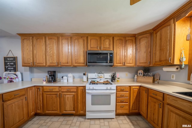 611 E Ash St, Canton, IL 61520 - kitchen with stainless steel microwave, white range with gas stovetop, brown cabinets, light countertops, and stone finish flooring