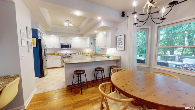 1119 W Brookforest Dr, Peoria, IL 61615 - kitchen with stainless steel appliances, a peninsula, a chandelier, white cabinets, and a raised ceiling
