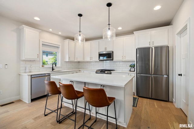 2821 W Lake Trail Ct, Dunlap, IL 61525 - kitchen featuring stainless steel appliances, decorative backsplash, white cabinets, a kitchen island, and light wood-type flooring