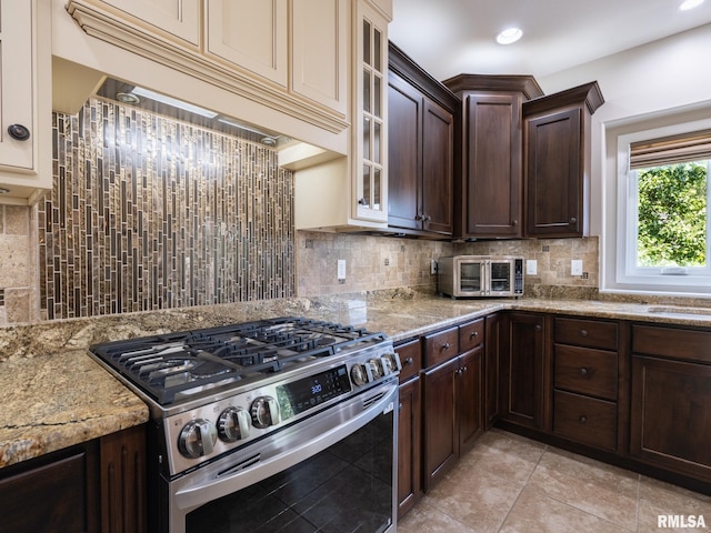 11014 N Saddlehorn Way, Dunlap, IL 61525 - kitchen with gas range, under cabinet range hood, dark brown cabinetry, decorative backsplash, and glass insert cabinets