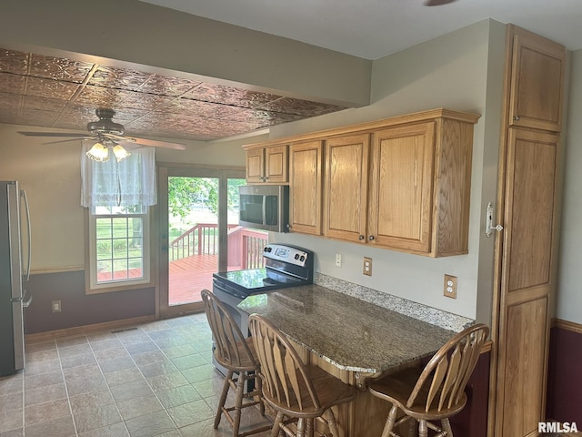 146 W Locust St, Canton, IL 61520 - kitchen with appliances with stainless steel finishes, ceiling fan, an ornate ceiling, a breakfast bar area, and brown cabinetry