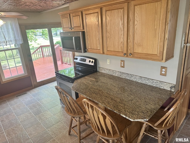 146 W Locust St, Canton, IL 61520 - kitchen with stainless steel microwave, electric stove, a breakfast bar area, dark stone counters, and brown cabinetry