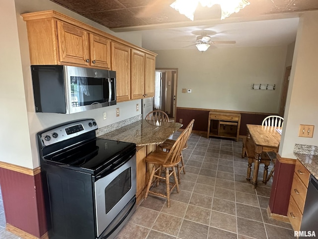 146 W Locust St, Canton, IL 61520 - kitchen featuring stainless steel appliances, tile patterned floors, wainscoting, a ceiling fan, and a breakfast bar