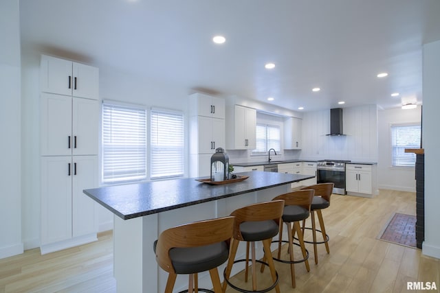 2129 Fondulac Dr, East Peoria, IL 61611 - kitchen with stainless steel stove, wall chimney exhaust hood, a breakfast bar area, a kitchen island, and light wood finished floors