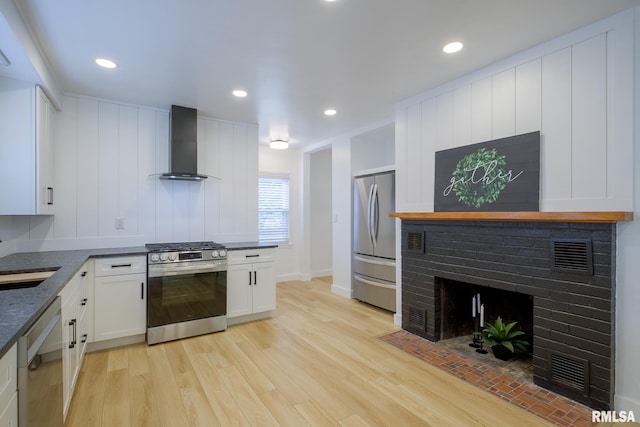 2129 Fondulac Dr, East Peoria, IL 61611 - kitchen featuring wall chimney range hood, stainless steel appliances, white cabinets, light wood-style flooring, and a fireplace