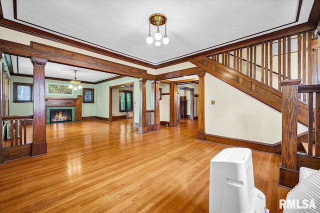 1027 N Maplewood Ave, Peoria, IL 61606 - unfurnished living room with a chandelier, ornamental molding, light wood-style floors, a warm lit fireplace, and ornate columns