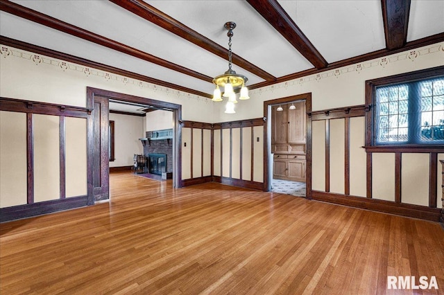 1027 N Maplewood Ave, Peoria, IL 61606 - spare room with light wood-style floors, beamed ceiling, and a brick fireplace