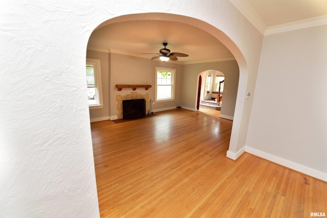 300 E Embert Pl, Peoria, IL 61603 - unfurnished living room featuring a ceiling fan, crown molding, light wood-style floors, a fireplace with flush hearth, and arched walkways